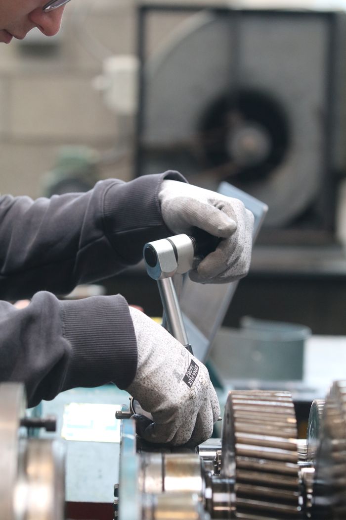 Male worker using tools on machinery in an industrial workshop setting.
